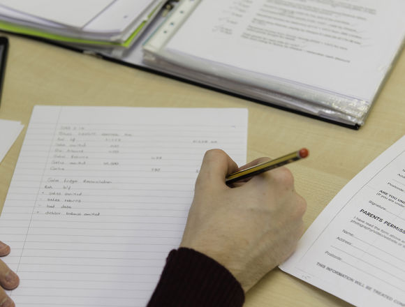 Close up of student working, with papers and a calculator scattered on the desk.